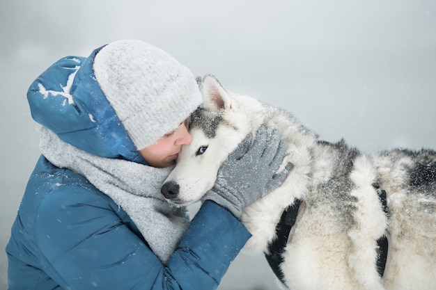 Mulher abraçando o husky siberiano nevado no inverno