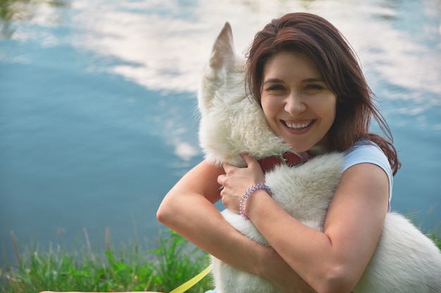 Mulher abraçando seu cachorro, tocando seu pêlo macio com as mãos e o rosto com água refletindo