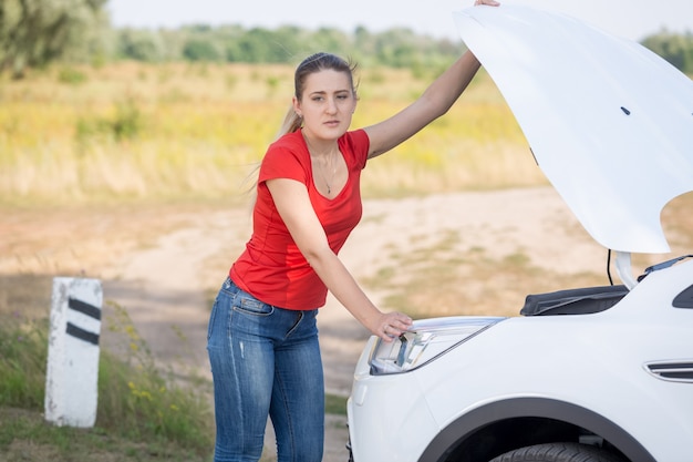 Mulher abrindo o capô do carro quebrado na beira da estrada