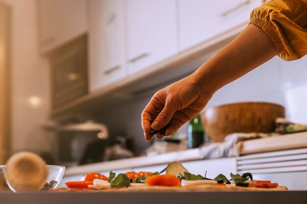 Mulher adicionando ingredientes saudáveis à pizza. Conceito feito em casa.