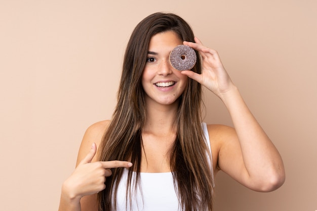 Foto mulher adolescente sobre parede isolada, segurando uma rosquinha e feliz