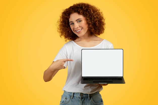 Foto mulher adolescente sorridente apontando o dedo para a tela vazia do laptop