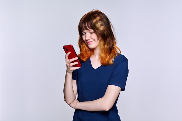 Mulher adolescente sorridente olhando para a tela do smartphone no fundo claro do estúdio