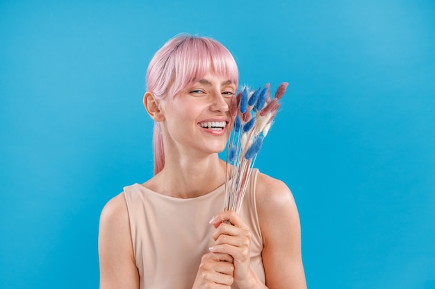 Mulher adorável com cabelo rosa sorrindo para a câmera segurando grama seca dos pampas posando