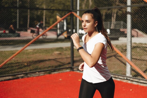 Foto mulher adorável jovem correndo em um parque esportivo lá fora. retrato de vista lateral correndo ao ar livre.