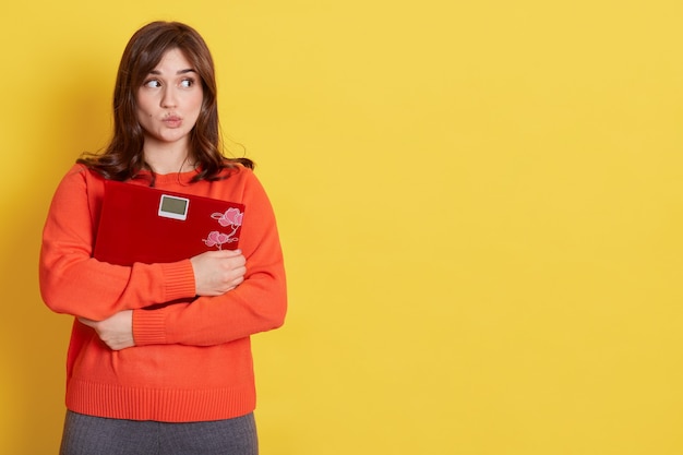 Mulher adorável sentindo-se perplexa e confusa, duvidando, pesando, vestindo um macacão laranja casual