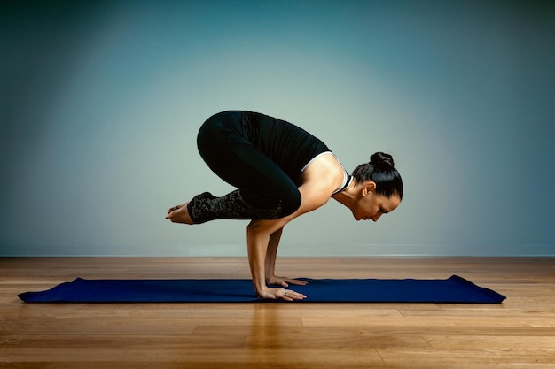 Mulher adulta, 45-55 anos de idade em boa forma, fazendo ioga, posando em um fundo azul do estúdio, com um piso de madeira sobre uma esteira de treinamento. ioga, alongamento, estilo de vida saudável.