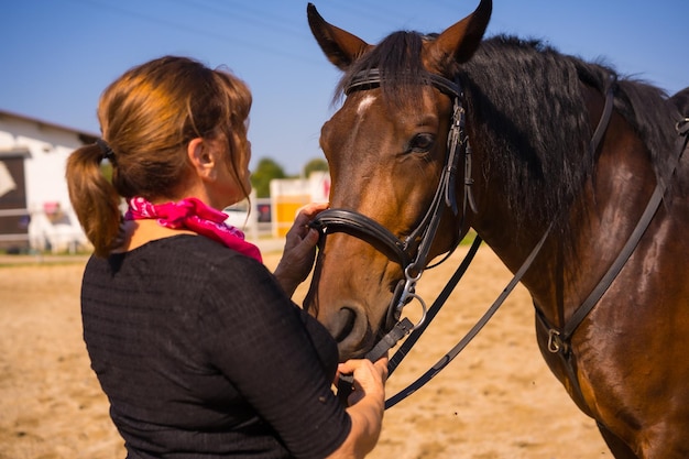 Mulher adulta a cavalo acariciando um cavalo marrom, vestida com roupas sul-americanas