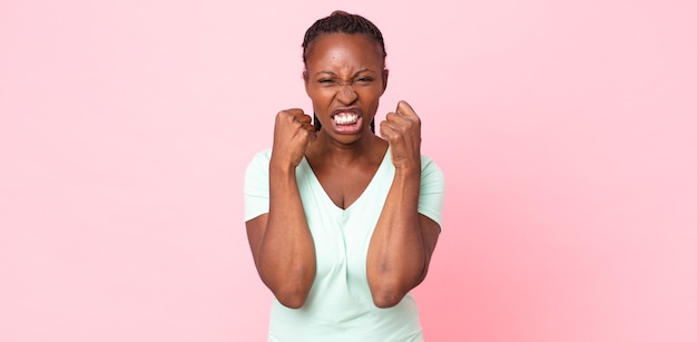 Mulher adulta afro-negra gritando agressivamente com olhar irritado, frustrado e irritado e punhos cerrados, sentindo-se furiosa