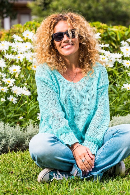 Mulher adulta caucasiana bonita feliz e alegre desfrutar do parque e sorrir para a câmera com margarida natural verde na superfície