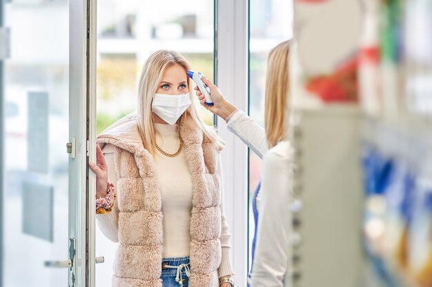 mulher adulta com máscara médica passando por procedimento covid-19 antes de entrar no supermercado