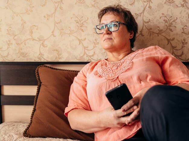 Mulher adulta com óculos em casa na cama com um telefone.
