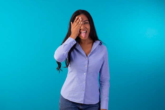 Mulher adulta com roupa formal, vestindo camisa azul e calça jeans em foto de estúdio com fundo azul.