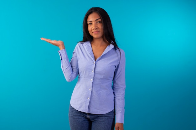 Mulher adulta com roupa formal, vestindo camisa azul e calça jeans em foto de estúdio com fundo azul.