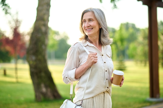 Mulher adulta com um sorriso pensativo e café