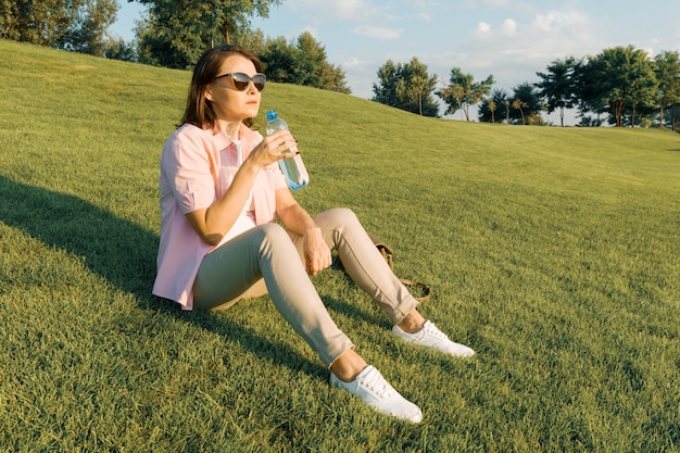 Mulher adulta em óculos de sol bebe água da garrafa