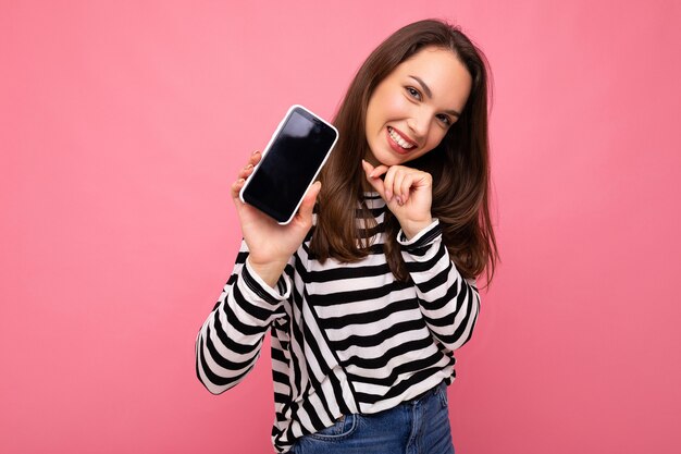 Mulher adulta engraçada encantadora vestindo um suéter listrado isolado na parede com espaço de cópia mostrando a tela do telefone móvel. Mock up, cutout