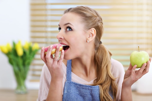 Mulher adulta escolhendo entre lanche saudável e não saudável na cozinha