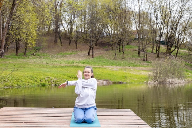 Mulher adulta faz ginástica para articulações na margem de um lago em um parque