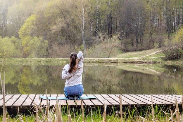 Mulher adulta faz ioga no lago no parque