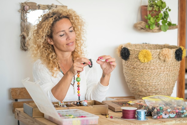 Mulher adulta fazendo joias artesanais em casa com miçangas e cordões coloridos