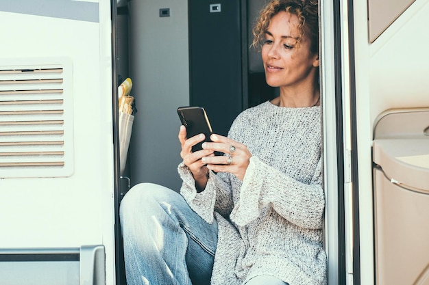 Mulher adulta independente sentada na porta de sua caminhonete moderna usa conexão de telefone celular e sorri Mulher alegre com viagens e tecnologia atividade de lazer