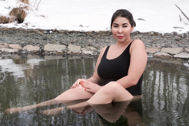 Mulher adulta jovem de tamanho grande em traje de banho preto sentado e tomando banho na piscina ao ar livre no spa
