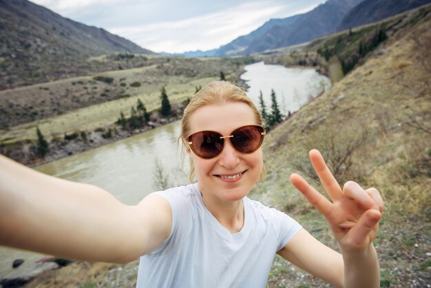 Mulher adulta jovem feliz em óculos de sol tira uma selfie, rindo para a câmera. viagem, blogs