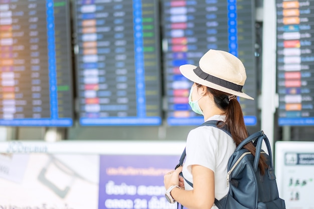 Mulher adulta jovem usando máscara cirúrgica no terminal do aeroporto, infecção por doença de Coronavirus (Covid-19) de proteção, mulher asiática com chapéu pronto para viajar. Novo conceito normal e bolha de viagens