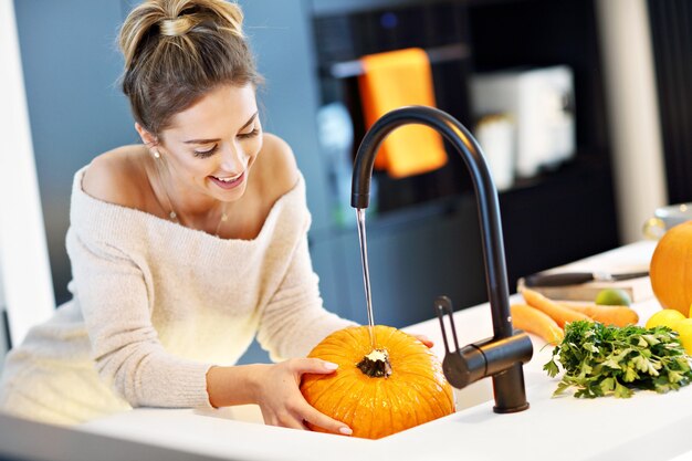 mulher adulta lavando abóbora na cozinha para o Halloween