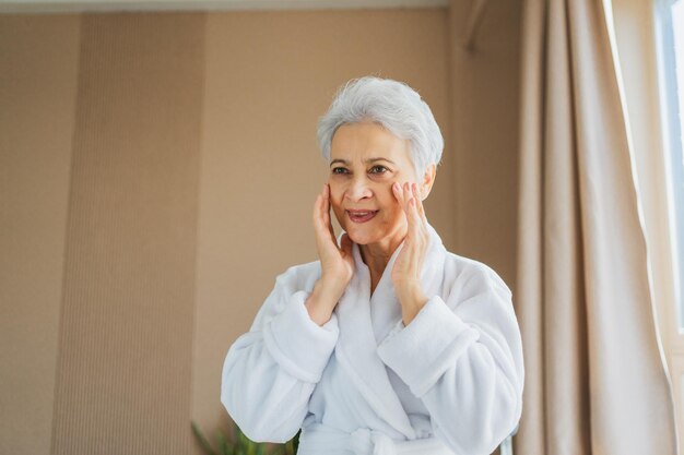 Mulher adulta madura aplicando creme facial anti-envelhecimento fazendo rotina diária de beleza sênior