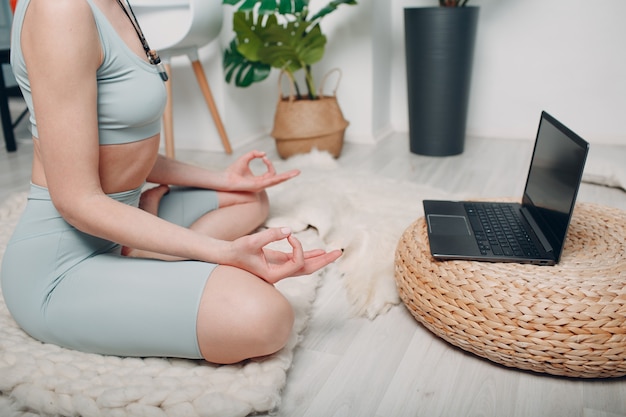 Mulher adulta madura fazendo ioga na sala de estar de casa com tutoriais on-line no laptop