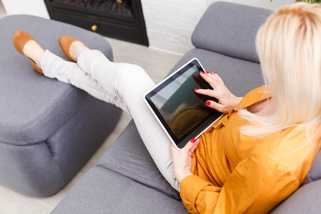 mulher adulta meada sentada no sofá com o tablet pc. Forma horizontal, vista frontal, espaço de cópia