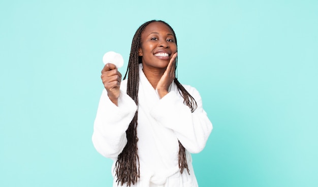 Mulher adulta negra afro-americana de roupão e segurando um algodão para limpeza de rosto