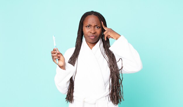 Mulher adulta negra afro-americana de roupão e segurando uma escova de dentes