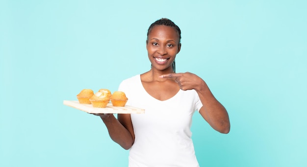 Mulher adulta negra afro-americana segurando uma bandeja de muffins