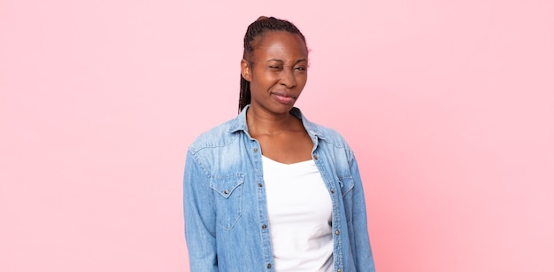 Mulher adulta negra parecendo feliz e amigável, sorrindo e piscando um olho para você com uma atitude positiva