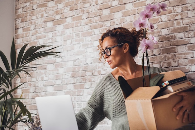 Mulher adulta perdeu o emprego e moveu suas coisas da mesa pessoas adultas do sexo feminino com caixa e coisas pessoais dentro na frente do computador portátil e local de trabalho estilo de vida do escritório e negócios de carreira