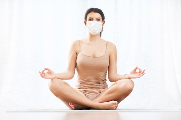 mulher adulta praticando ioga com máscara em casa