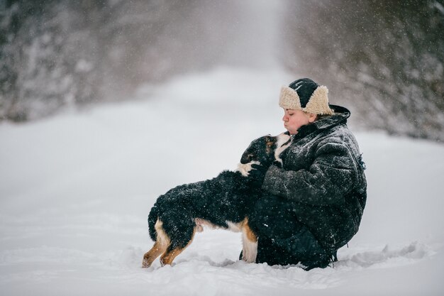 Mulher adulta que abraça o cão adorável na estrada do inverno ao ar livre.