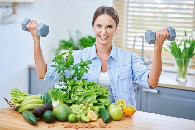 Mulher adulta saudável com comida verde na cozinha