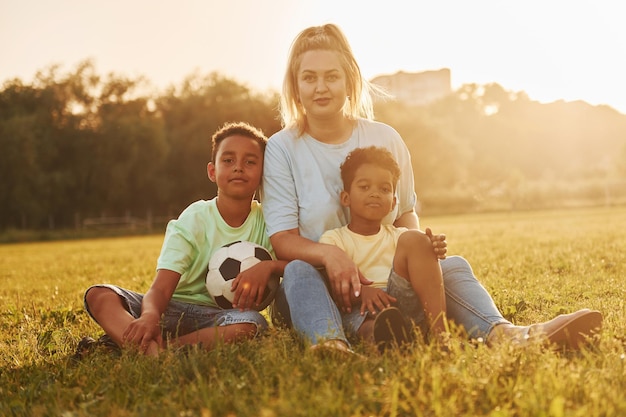 Mulher adulta senta-se com duas crianças negras no campo no dia de verão