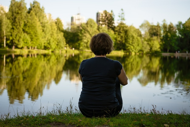 Mulher adulta sentada perto do lago deu as costas