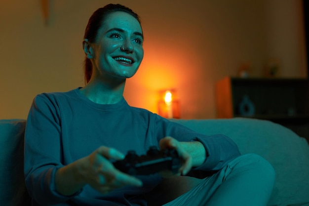 Mulher adulta sorridente jogando videogames no escuro e segurando o controlador