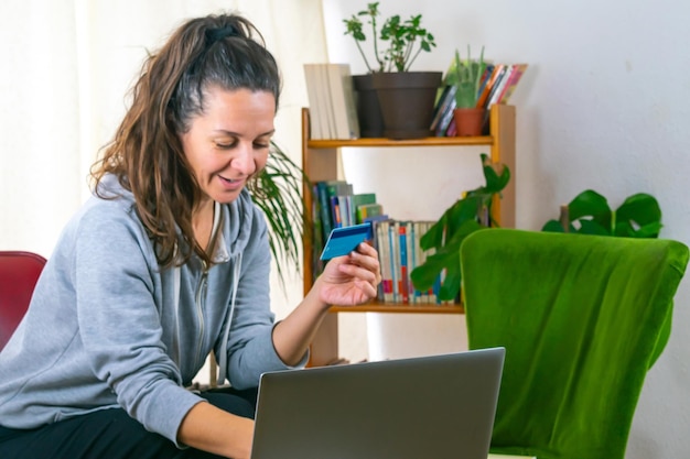 Foto mulher adulta sorridente segurando um cartão bancário enquanto olha para o seu computador, tecnologia financeira, espaço de cópia