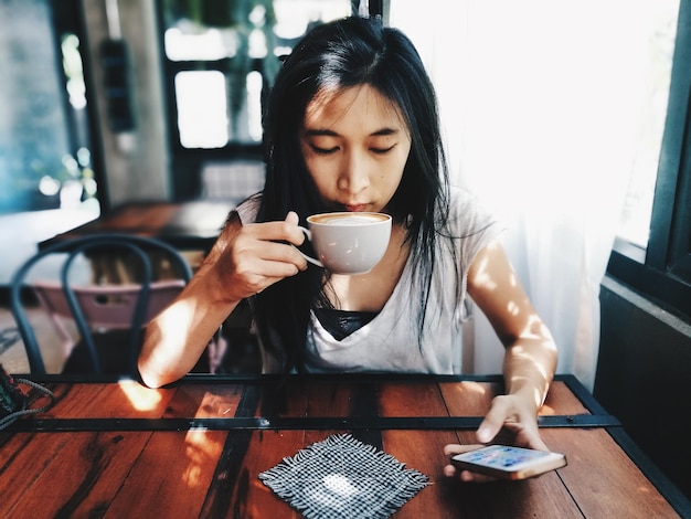 Foto mulher adulta usando telefone enquanto bebe café em um café