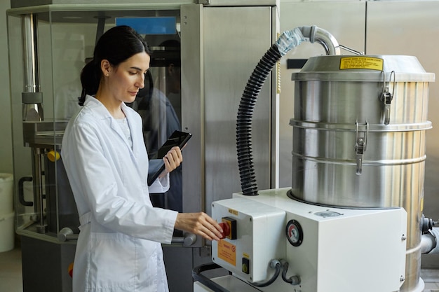 Mulher adulta vestindo um casaco de laboratório usando uma unidade de máquina em uma oficina de fábrica limpa