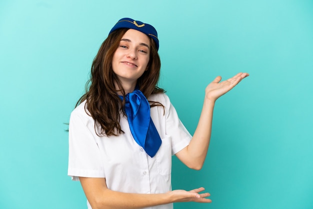 Mulher aeromoça isolada em fundo azul estendendo as mãos para o lado para convidar para vir