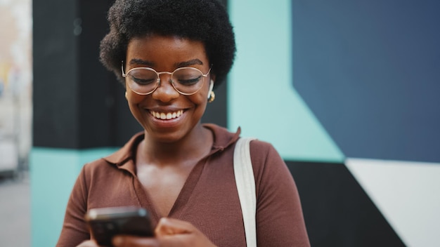 Foto mulher africana andando na cidade usando seu smartphone e smili