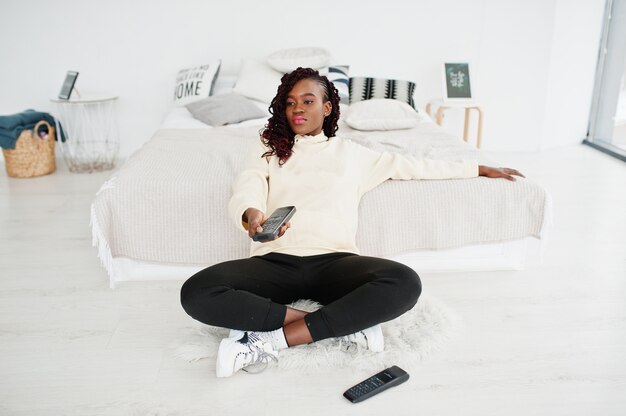 Mulher africana assistindo tv em casa e segurando um controle remoto na cama